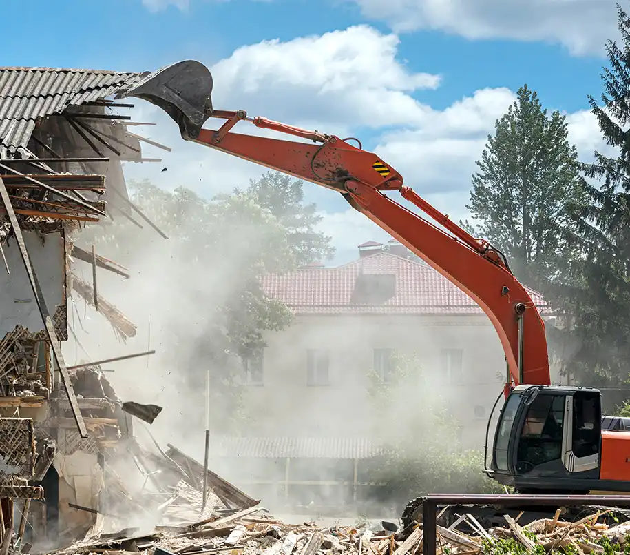 Bagger wirbelt neben Siedlung bei Abrissarbeiten an Schutthaufen Staub auf