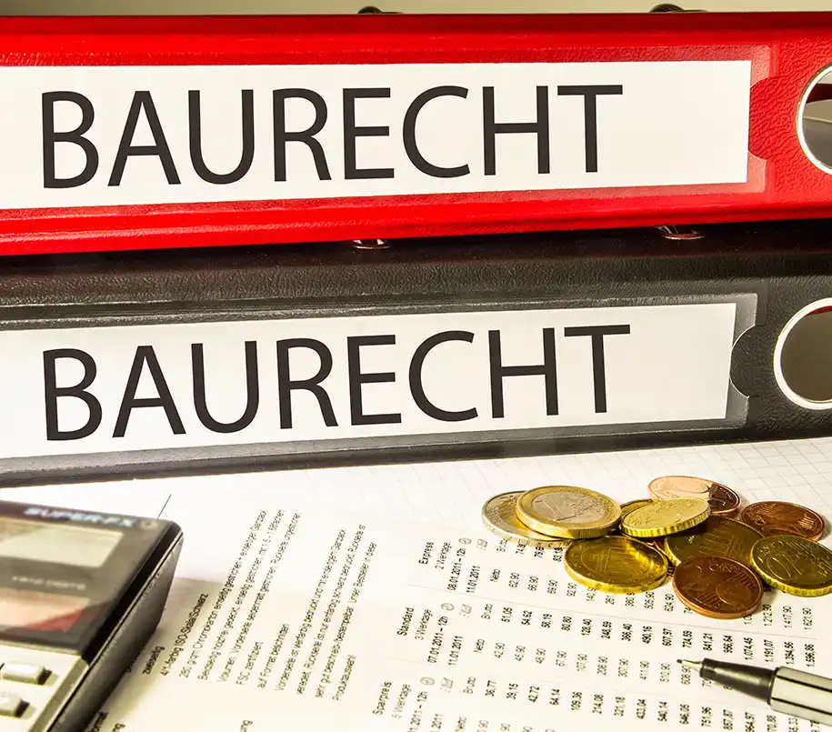 Zwei Aktenordner mit Titel "Baurecht" liegen über Dokumenten und Euromünzen